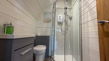 A modern bathroom with a glass shower enclosure, a toilet, and a vanity with a soap dispenser.