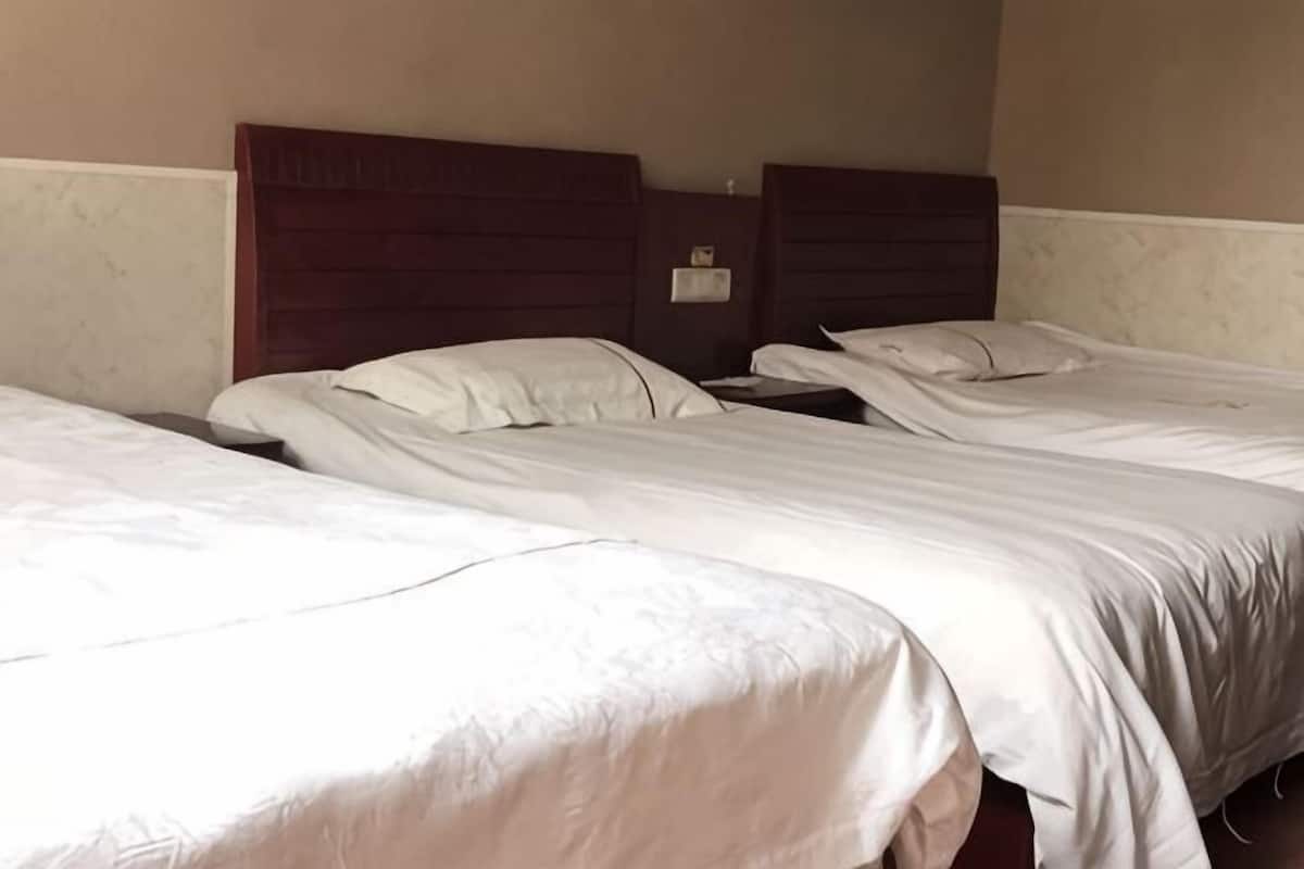 A hotel room with two single beds, wooden headboards, and a beige wall.