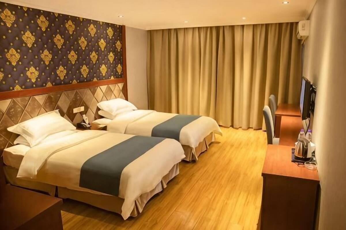 A hotel room with two beds, a desk, a TV, and a large window with curtains.