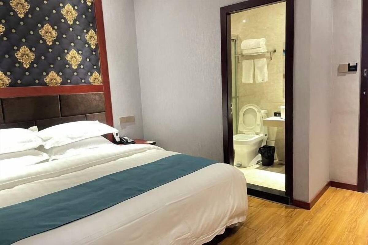 A hotel room with a bed, a bathroom visible through an open door, and a patterned wall.