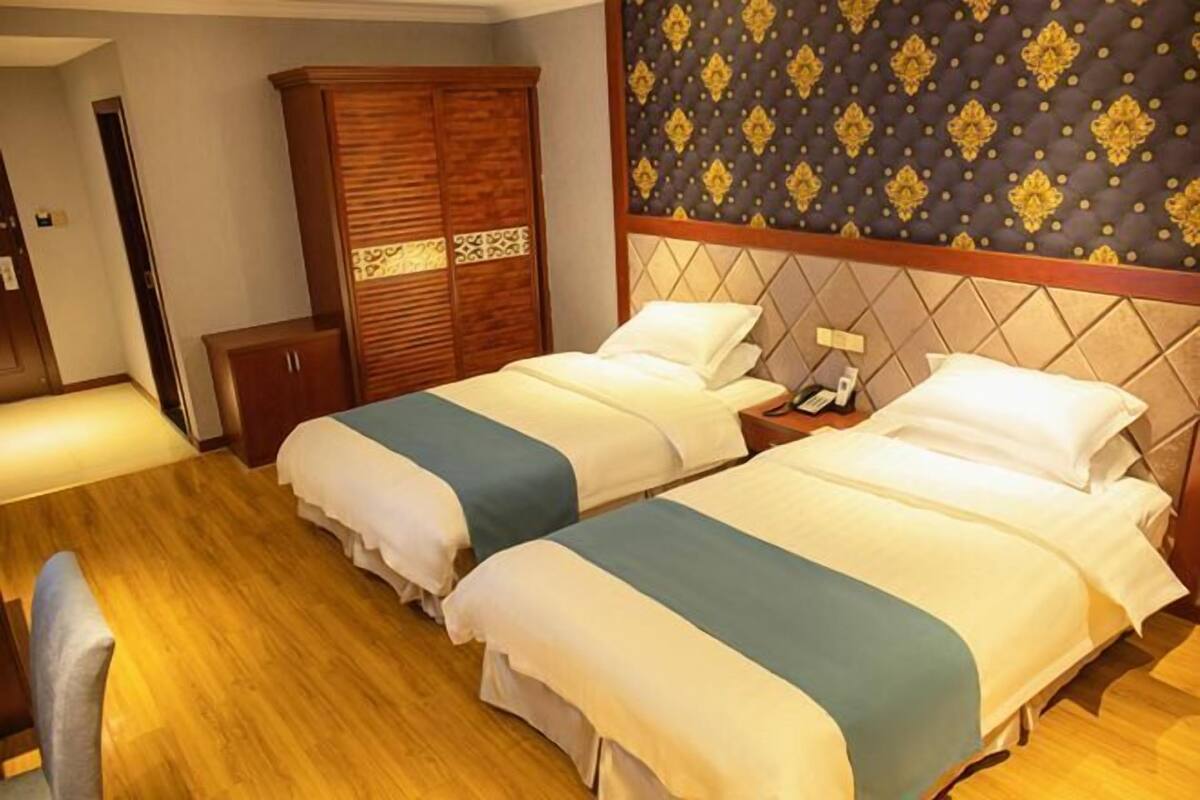 A hotel room with two beds, a wooden wardrobe, a nightstand, and a patterned headboard.