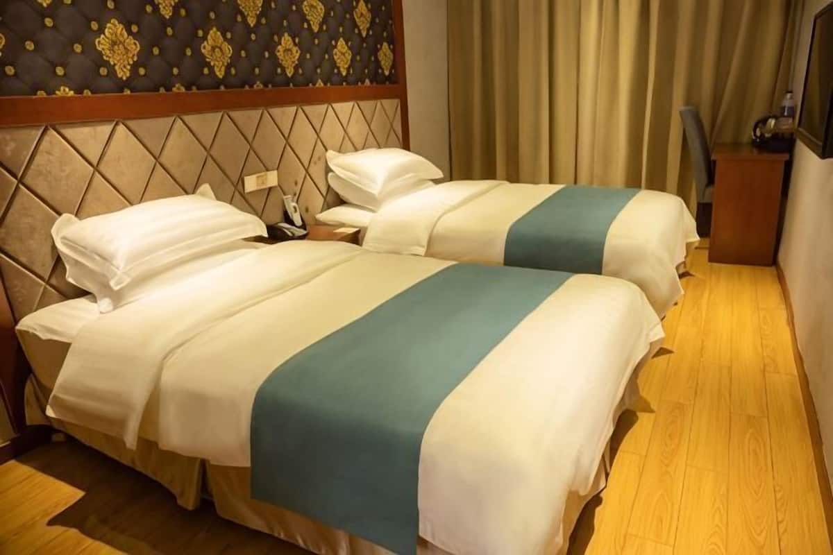 A hotel room with two beds, a wooden floor, a headboard with a patterned design, and a curtain.