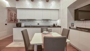 Una cocina moderna con armarios blancos, un microondas y un lavabo. Hay una mesa de comedor con sillas y una copa de vino encima.