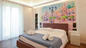 Un dormitorio con cama, una mesita de noche, una estantería y un cuadro de una escena callejera en la pared.