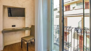 Habitación con televisor incorporado, una silla, una mesita y balcón con vistas a edificios cercanos.