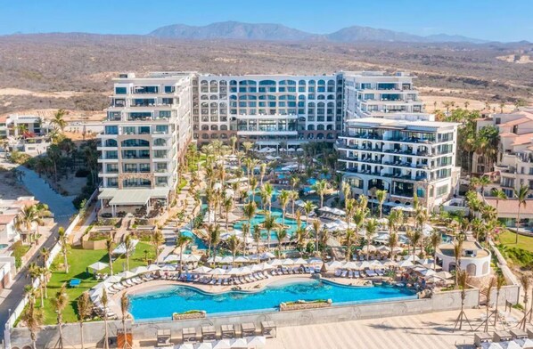 Un resort con varias piscinas, palmeras y montañas al fondo.