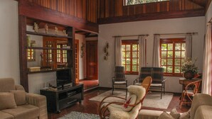 A living room with a television, sofas, wicker chairs, and a large window with curtains. - Casa Horto Village (Campos do Jordão)