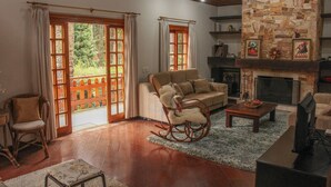 A living room with a stone fireplace, wooden flooring, a rocking chair, and a sofa. - Casa Horto Village (Campos do Jordão)
