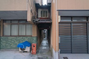 A narrow alleyway leading to a building with a garage door and a covered outdoor area with a heater. - 【Hoshizora inn】Machiya 1station from Kyoto Station (Kyoto)