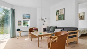 A modern living room with a sofa, a dining table, and a coffee table. There are two chairs, a lamp, and artwork on the walls. - Gudhjem Søpark Lejl. 51 (Gudhjem)