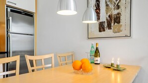 Ein Essbereich mit einem Holztisch, drei Stühlen, einer Orangenschale, zwei Weinflaschen und zwei Kerzen auf einem Tablett.