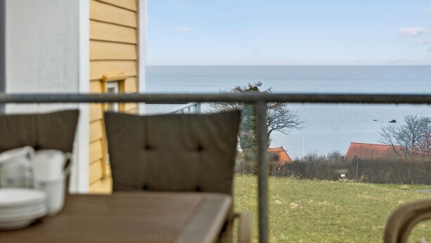 Ein Balkon mit Meerblick, ein Holztisch mit Kissen und ein Stuhl.