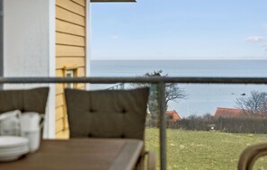 A balcony with a view of the sea, a wooden table with cushions, and a chair. - Gudhjem Søpark Lejl. 6 (Gudhjem)