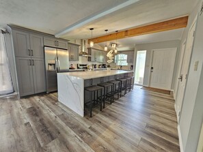 A modern kitchen with a large island, wooden flooring, and bar stools. - Siesta Key Charm - Pool, minutes to beach, private and spacious (Sarasota)