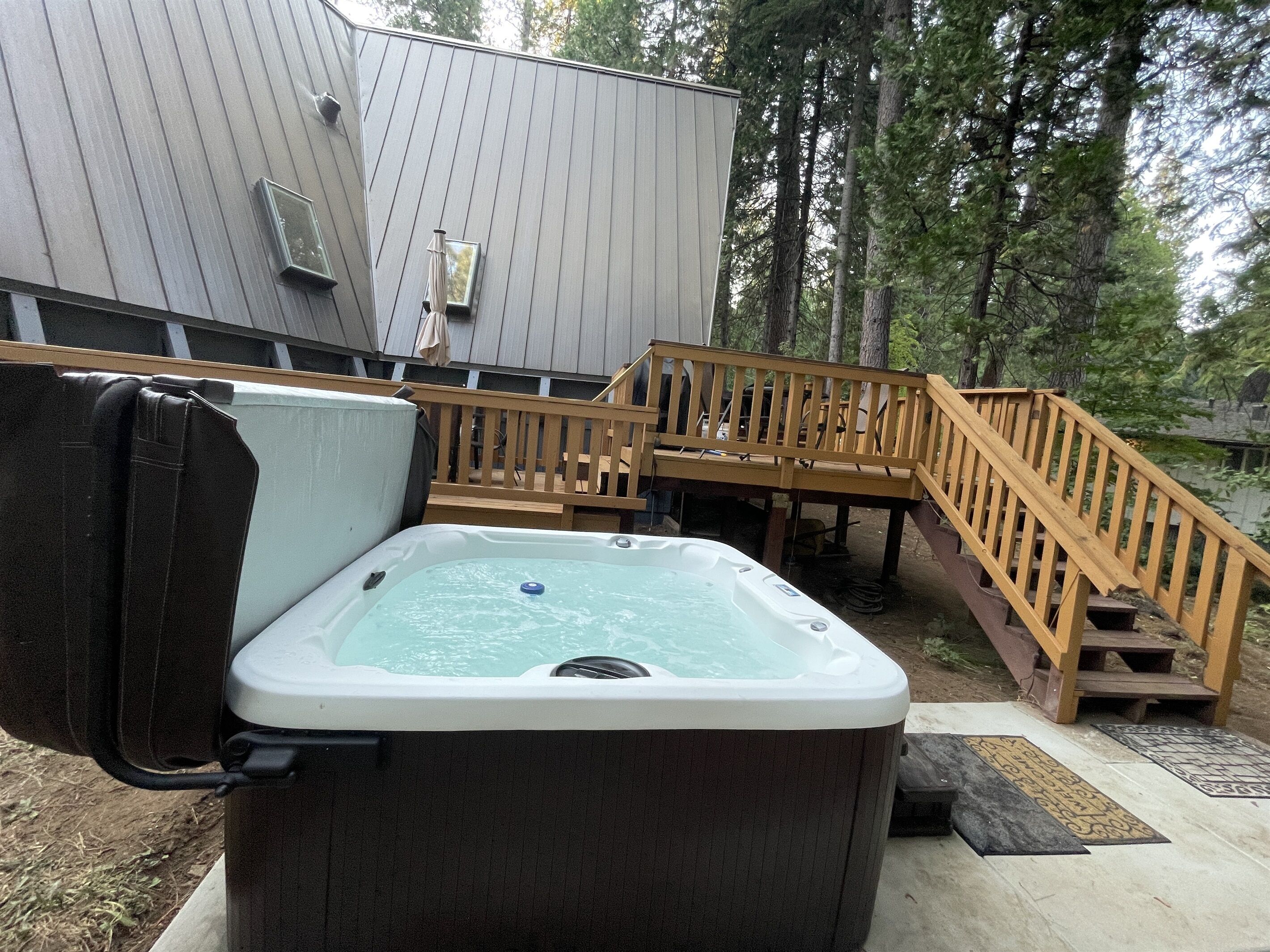 A hot tub outdoors with a wooden deck and stairs leading to a house.