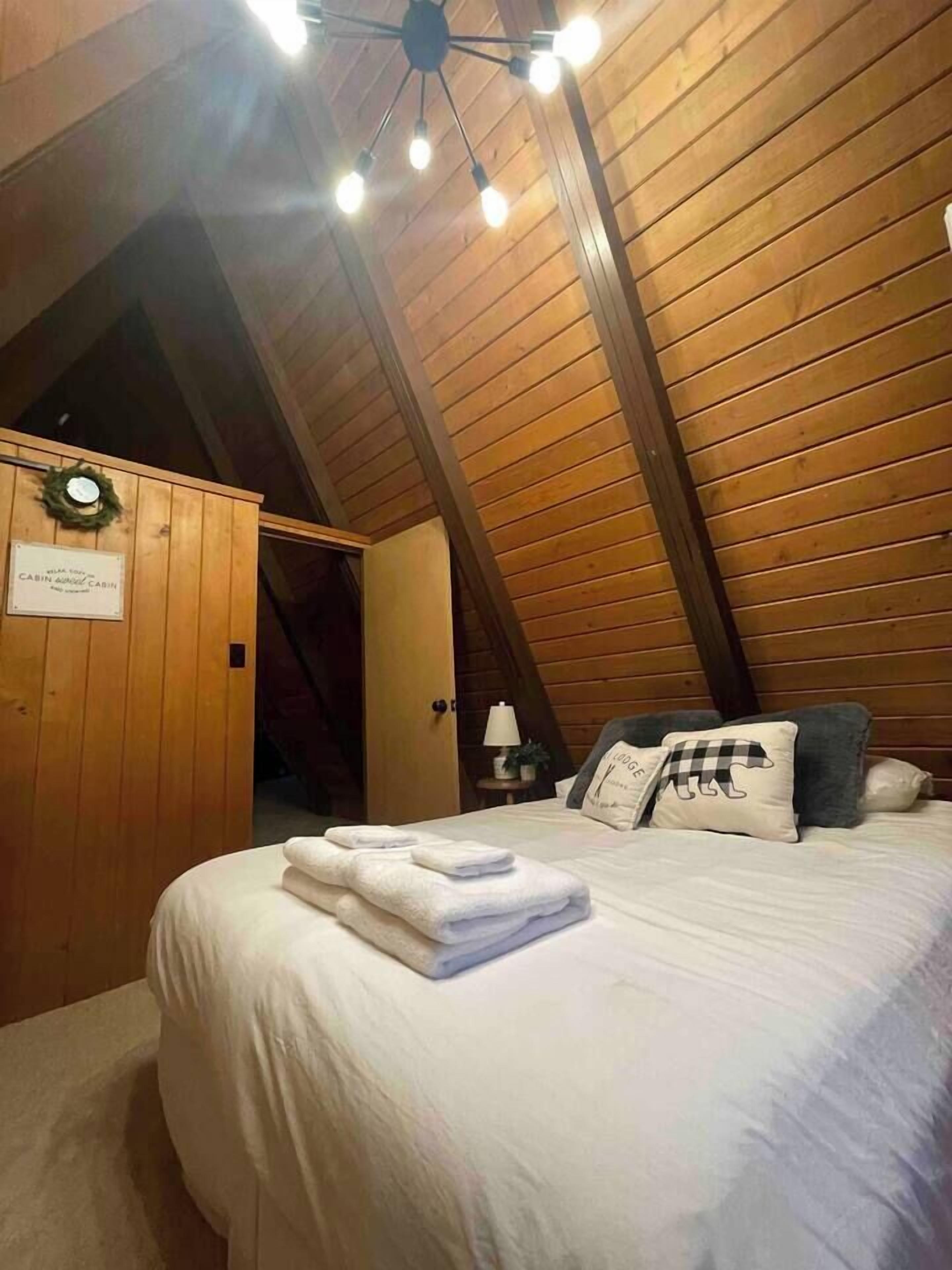 A cozy attic bedroom with a sloped ceiling, a bed with neatly folded towels, and a sign indicating it's a cabin.