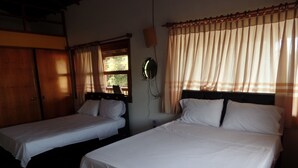 Two single beds with white linens in a room with wooden floors and a window with curtains.