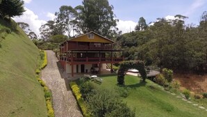 A two-story building with a balcony, surrounded by lush greenery and a paved pathway.