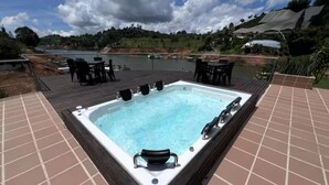 A hot tub on a wooden deck with a view of a lake and hills.