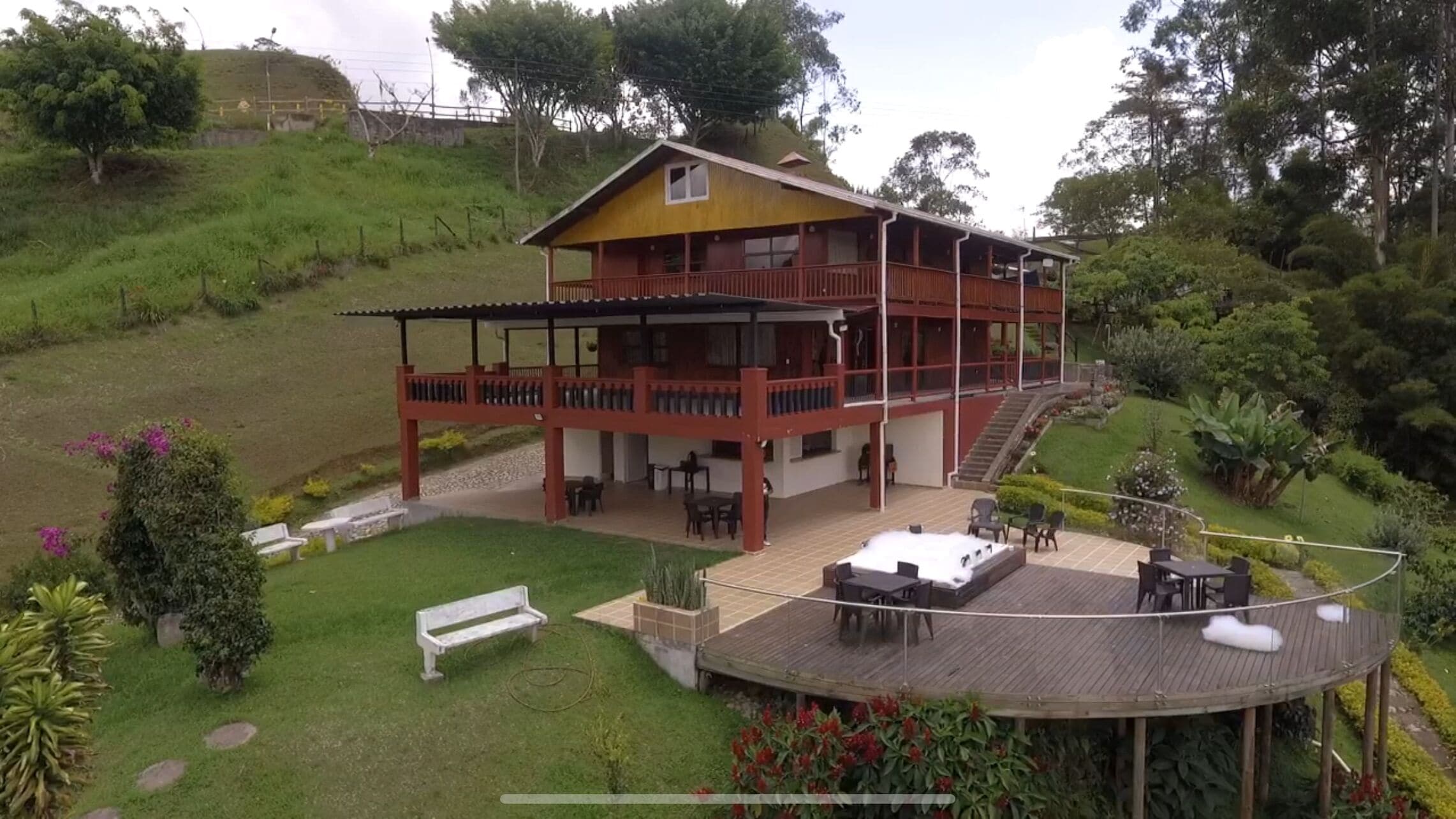A two-story wooden house with a balcony and a deck, surrounded by lush greenery.