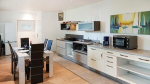 A modern kitchen with white cabinets, a dining area with a table set for two, and a painting of sailboats on the wall.