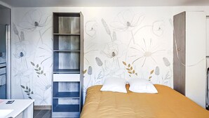 A bedroom with a bed, a wardrobe, a desk, and a shelving unit against the wall.