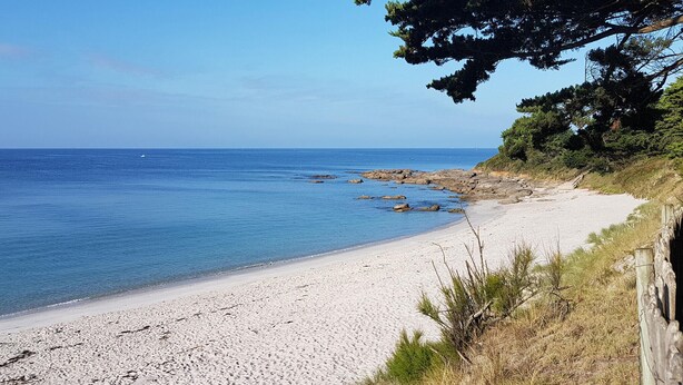 A beach with white sand, clear blue water, and rocky outcrops.
