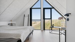 Un dormitorio con un tragaluz grande, una cama, una mesita de noche y vistas al exterior.