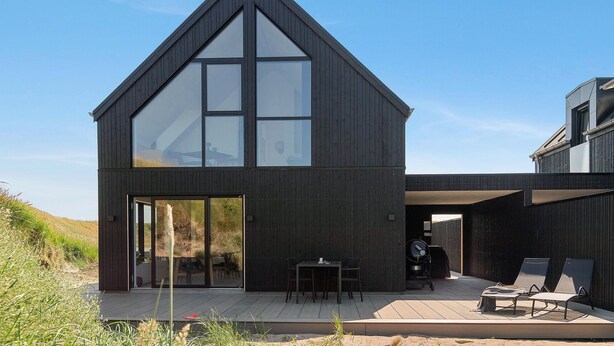 Una casa moderna con un amplio ventanal, un patio con mesa y sillas, y una zona de barbacoa.