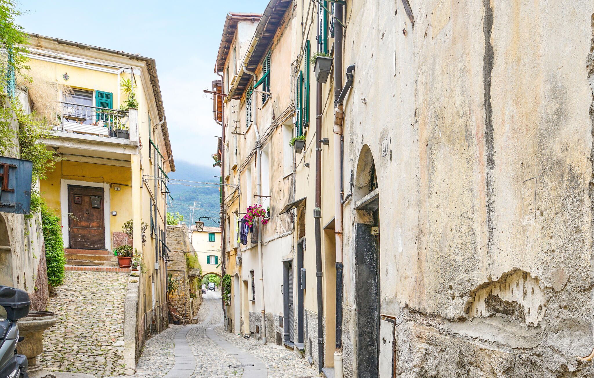A narrow cobblestone street flanked by historic buildings with balconies and outdoor plants.