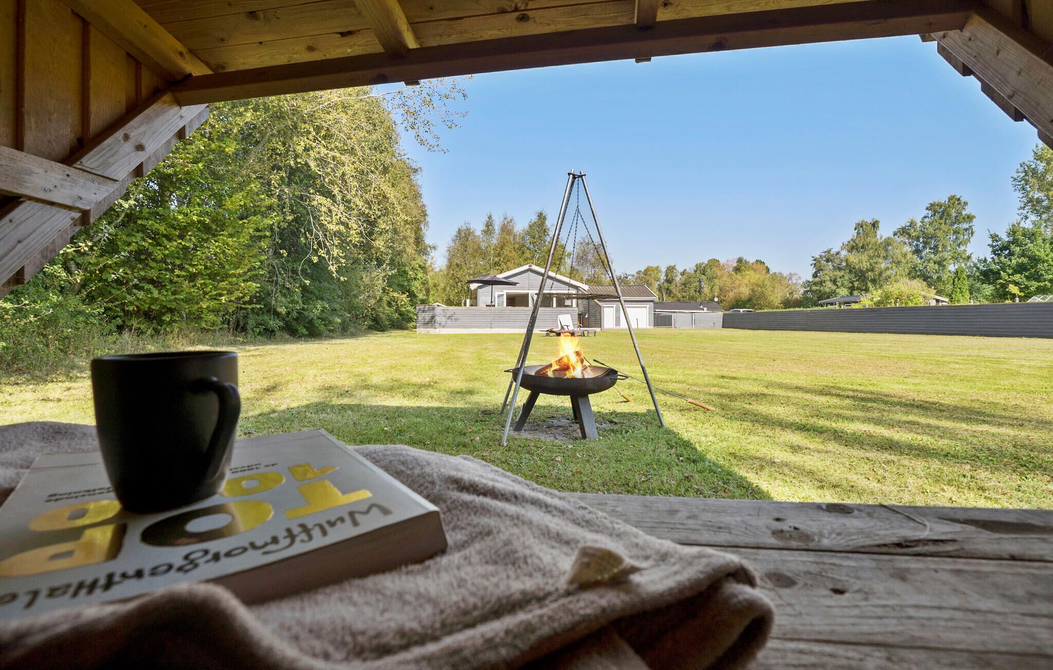 A picnic setup with a book, a mug, and a campfire in a backyard.