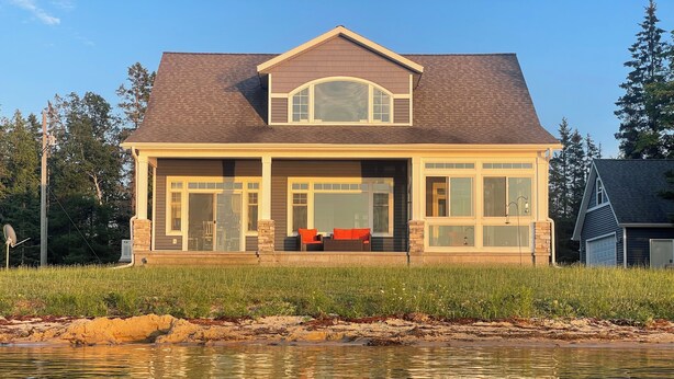 A two-story house with a large front porch, a garage, and a pond in the foreground.
