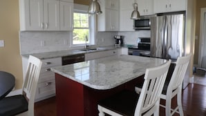 A kitchen with white cabinets, a granite countertop, stainless steel appliances, and a central island with bar stools.