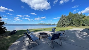 A lakeside patio with a fire pit, lounge chairs, and a small boat.