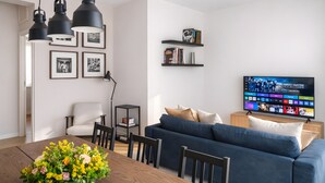 A modern living room with a blue sofa, a wooden dining table with a floral centerpiece, a TV on the wall, and black pendant lights. - Sunny Monteverde Escapes (ROMA)