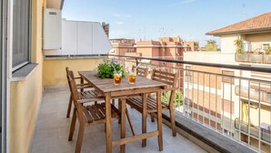A wooden balcony with a table and chairs, a potted plant, and a clear view of the surrounding buildings. - Sunny Monteverde Escapes (ROMA)