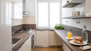 A modern kitchen with wooden flooring, white cabinets, a gas stove, and a window providing natural light. - Sunny Monteverde Escapes (ROMA)