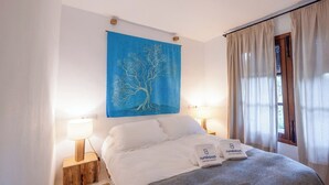 A bedroom with a bed, two bedside lamps, a blue wall tapestry, and a window with curtains. - Flor de Pita Jimena de la Frontera by Ruralidays (Cádiz)