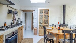 A compact kitchen with a gas stove, wooden cabinets, and a dining area with a table and chairs. - Flor de Pita Jimena de la Frontera by Ruralidays (Cádiz)