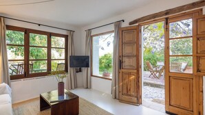 A room with a wooden door, a television, a white sofa, a coffee table, and a view of the outdoors. - Flor de Pita Jimena de la Frontera by Ruralidays (Cádiz)