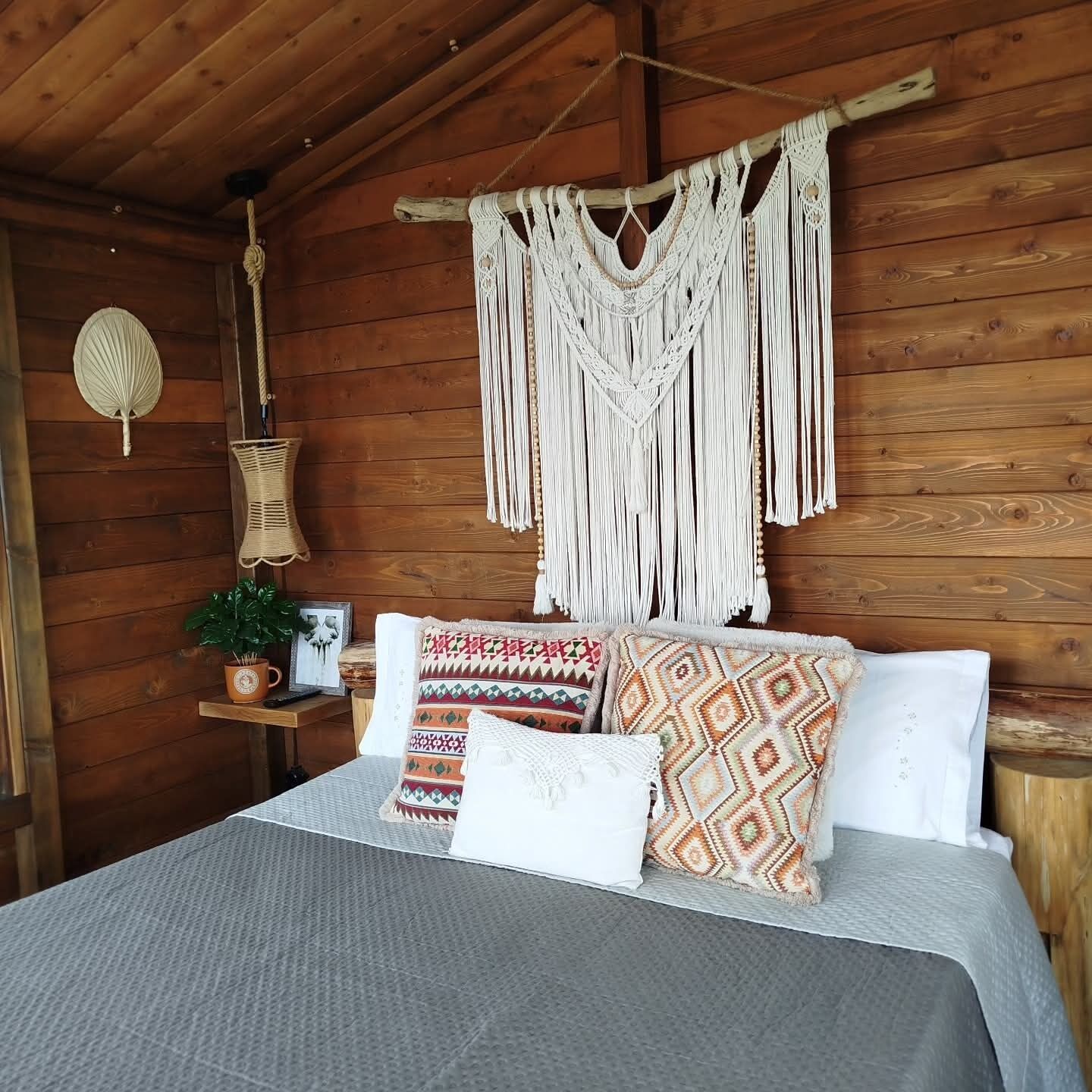 L’intérieur d’un chalet en bois, avec un lit, une décoration murale en macramé et une lanterne suspendue.
