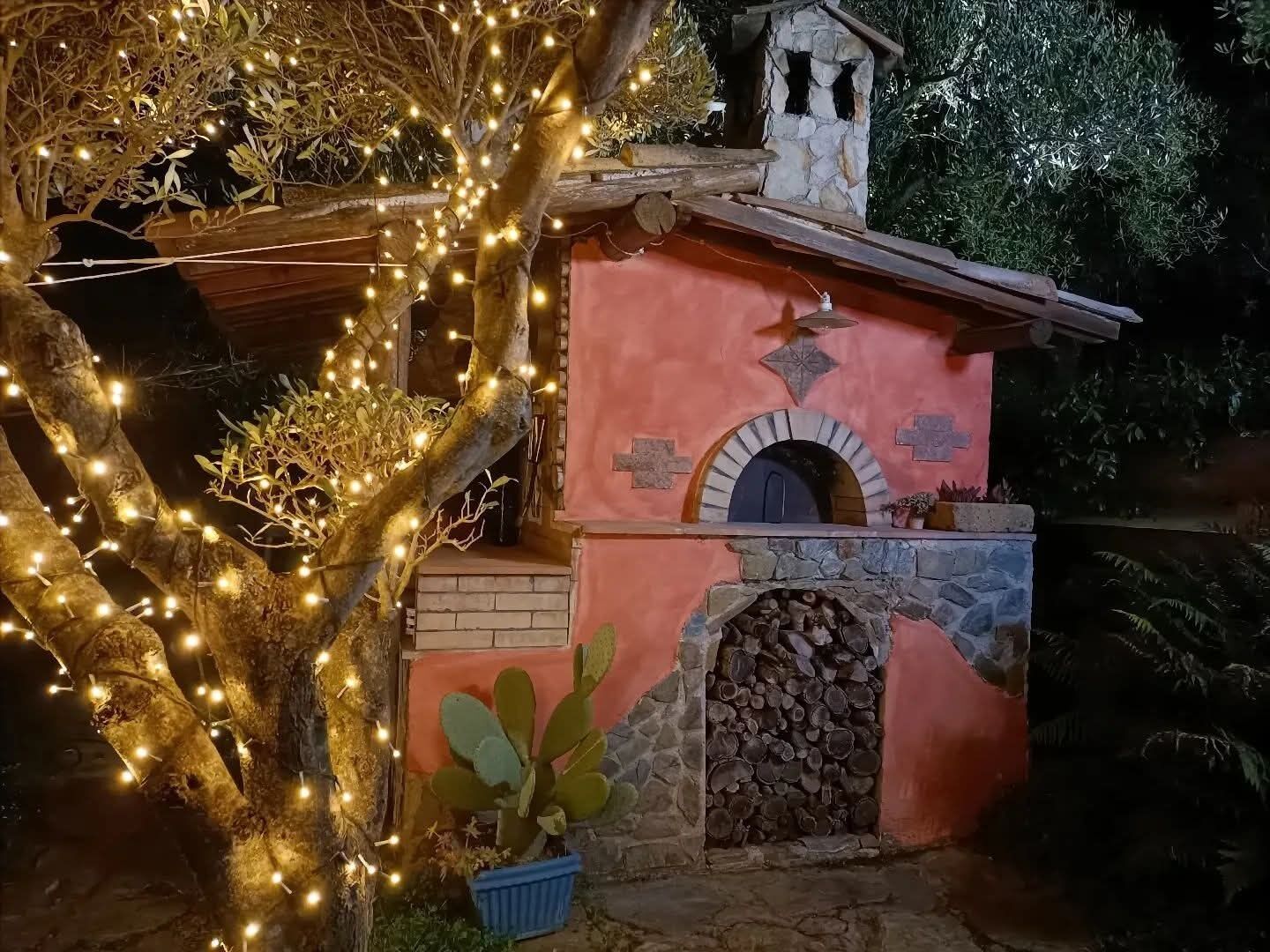 Un bâtiment rustique doté d’une cheminée en pierre, d’une petite entrée en arc de cercle et d’une structure en bois sur le toit.