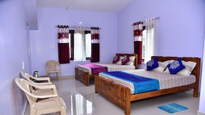 A bedroom with two beds, a wooden headboard, a small table, and two chairs. - Madhuvana Homestay Coorg  (Madikeri)