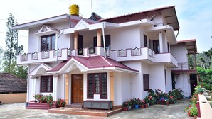 A two-story house with a balcony, a satellite dish, and potted plants. - Madhuvana Homestay Coorg  (Madikeri)