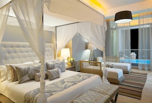 A luxurious bedroom with a canopy bed, a separate sitting area with a sofa and armchairs, and a view of a pool.