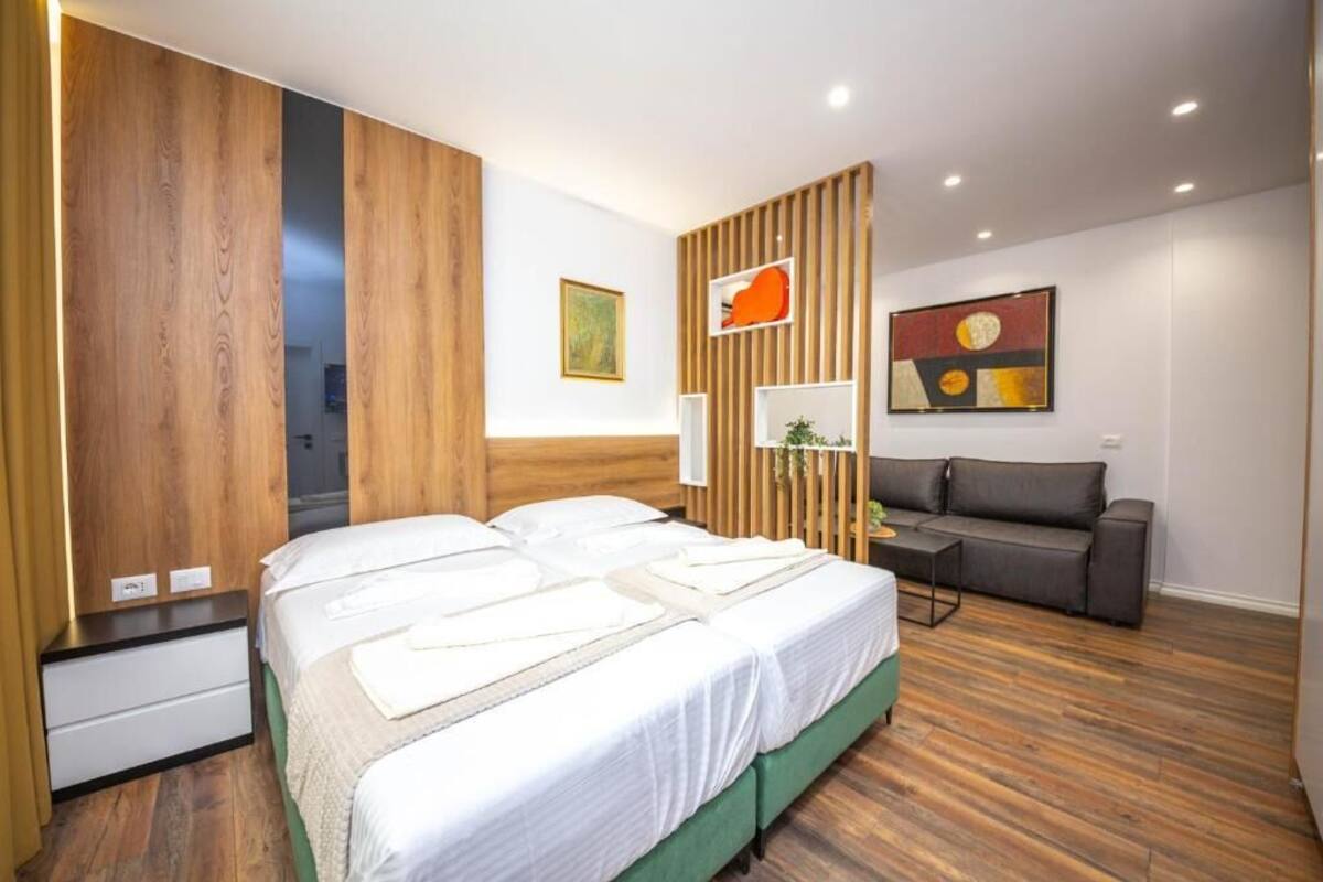 Une chambre d’hôtel moderne avec un grand lit, un canapé, des panneaux de bois et des œuvres d’art accrochées aux murs.