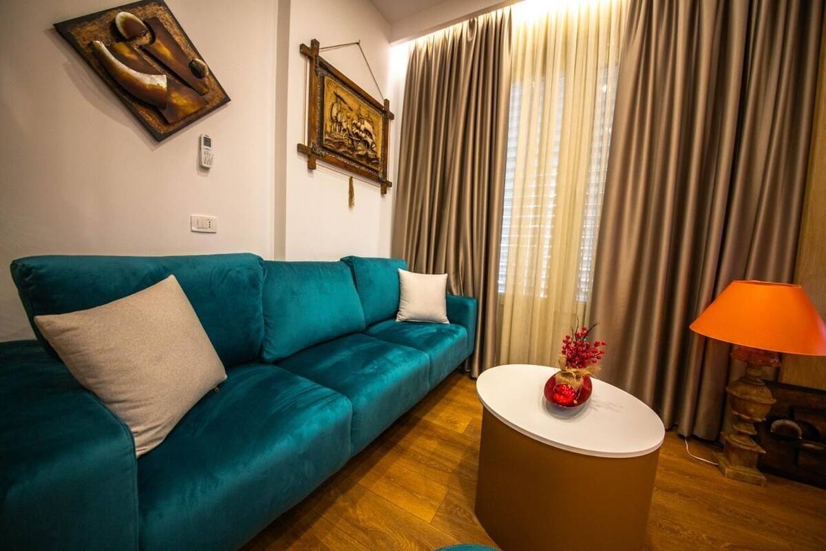 Un canapé de couleur bleu sarcelle avec un coussin blanc, une table basse ronde ornée d’un objet rouge et une lampe.