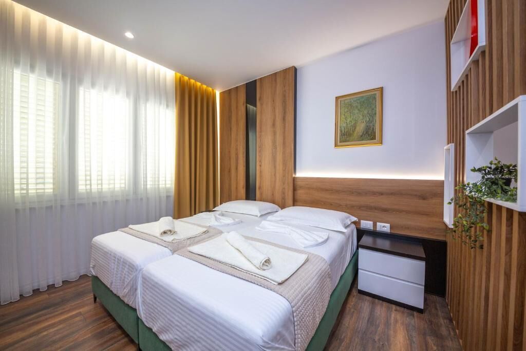 Una habitación de hotel con dos camas, una mesita de noche pequeña, un estante en la pared y un cuadro.
