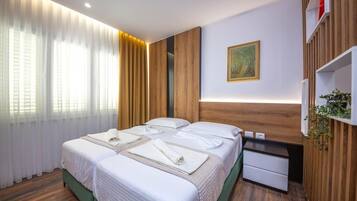 Una habitación de hotel con dos camas, una mesita de noche pequeña, un estante en la pared y un cuadro.
