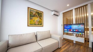 Ein modernes Wohnzimmer mit einem beigefarbenen Sofa, einem Gemälde an der Wand und einem Flachbildfernseher auf einem Holzständer.